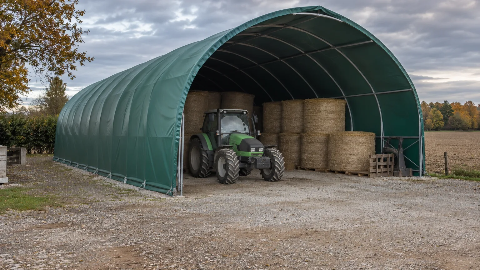 Tunnel de stockage agricole à bâche verte opaque abritant un tracteur et des balles de foin